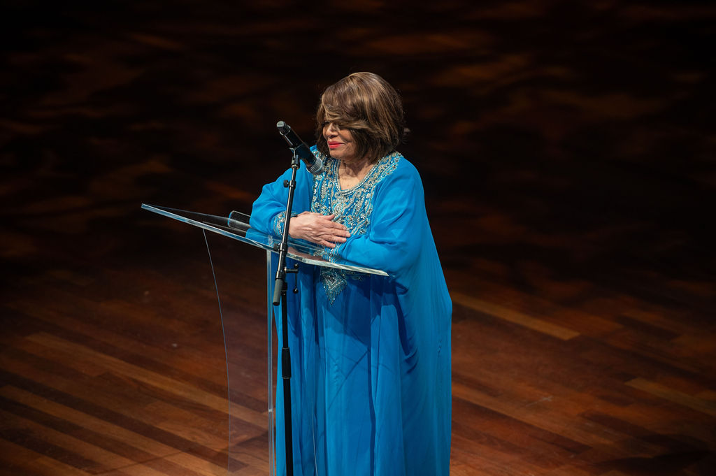 Speaker at podium in turquoise gown with hands over heart