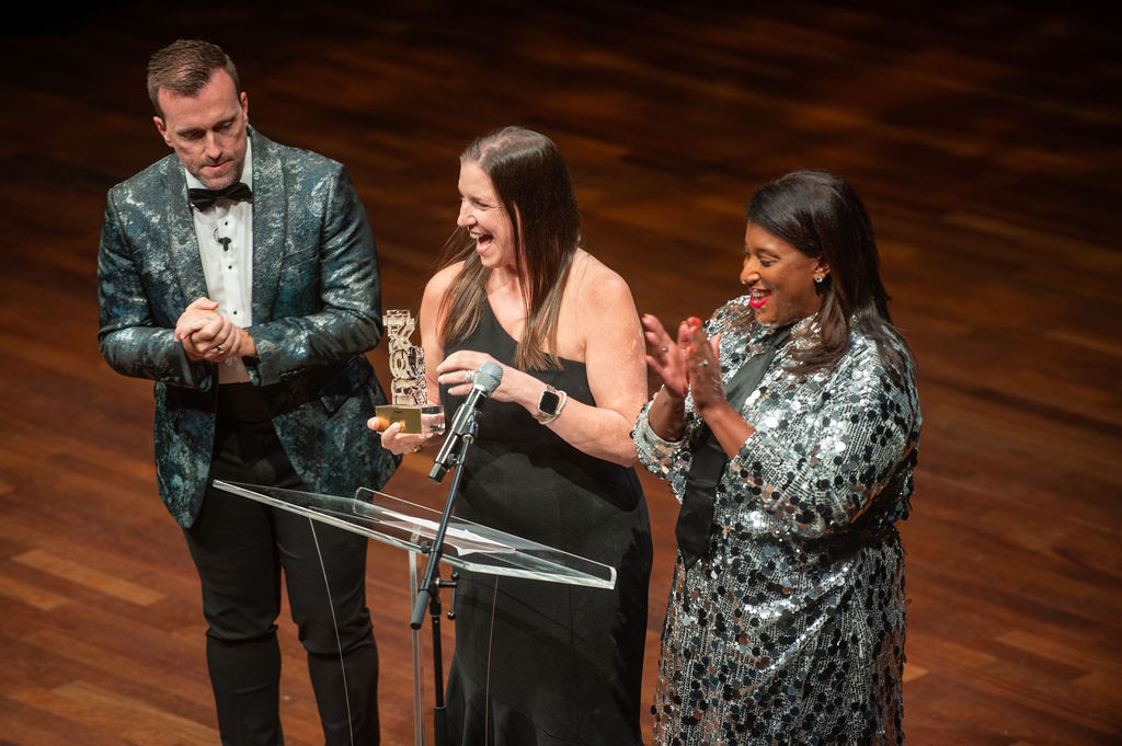 Woman receiving NEXT Award trophy on stage, laughing with joy