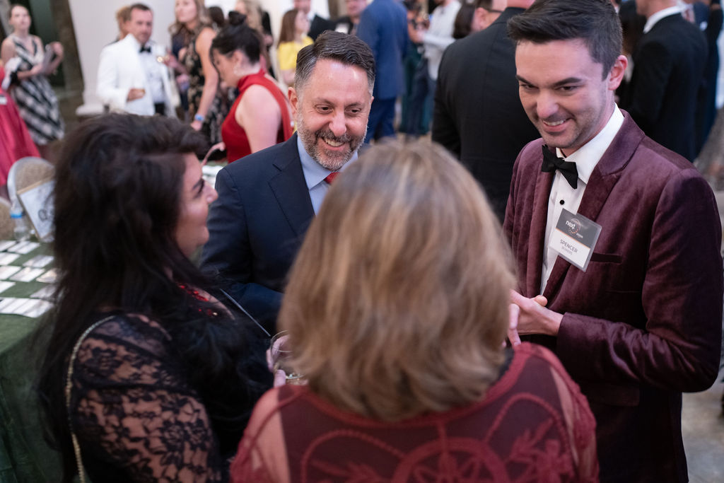 Three people laughing at a candlelit dinner table in velvet jackets