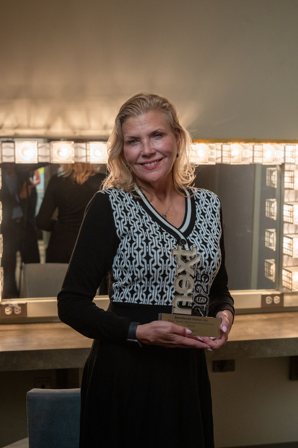 Woman holding NEXT trophy solo with warm smile in dressing room
