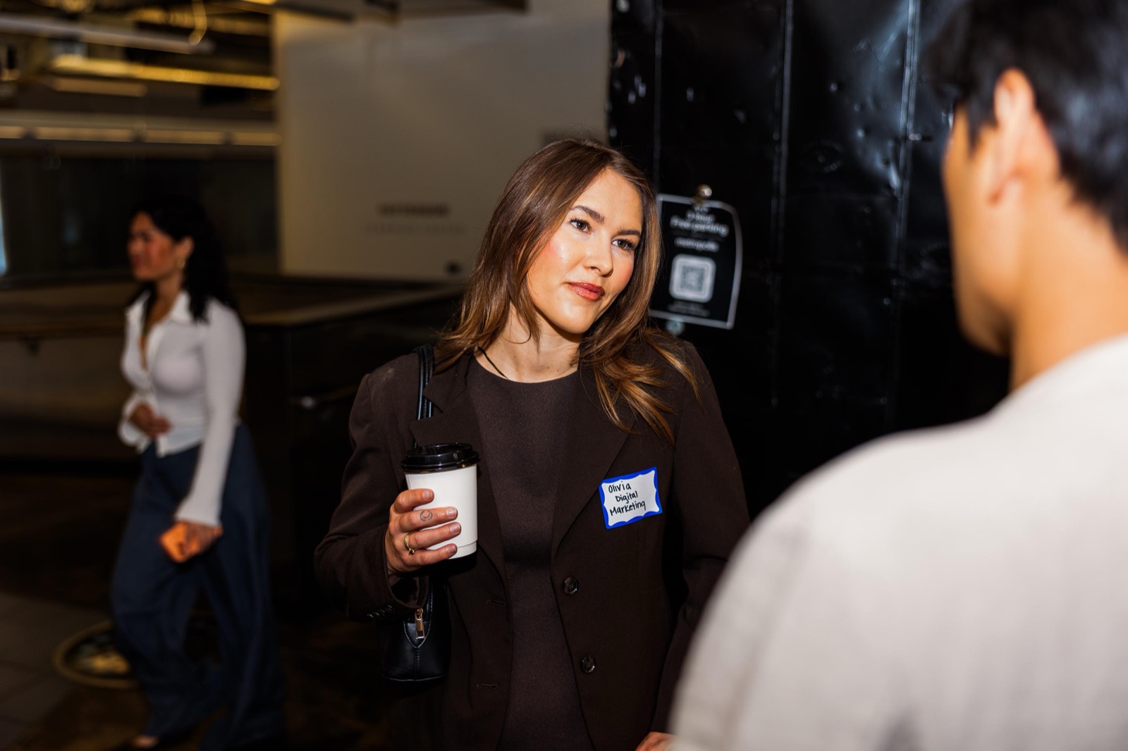 A member with a coffee cup and name tag mid-conversation in the EC lobby