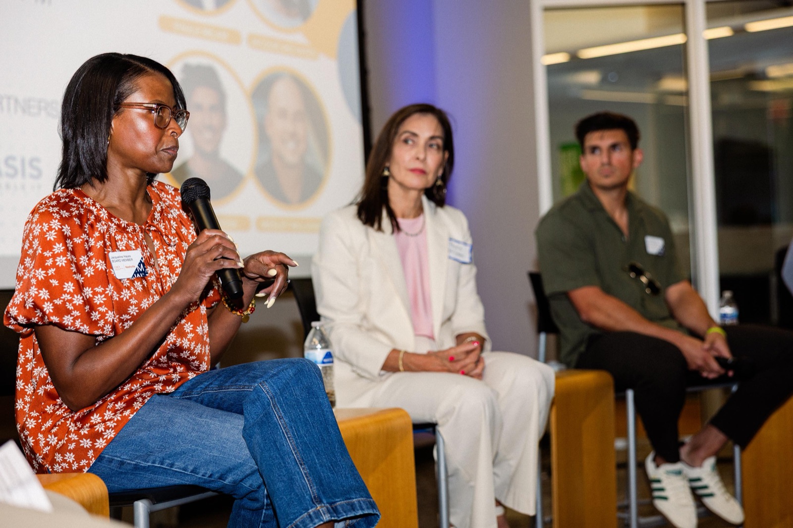 Three panelists seated on stage, one speaking into a microphone, at an EC lunch and learn