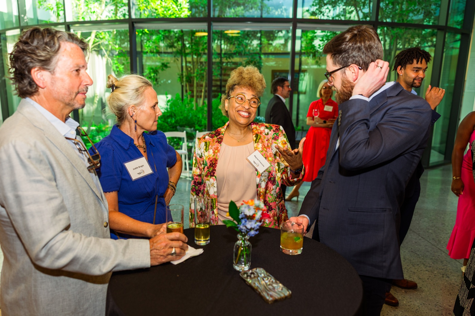 Five guests gathered around a cocktail table in front of a garden window