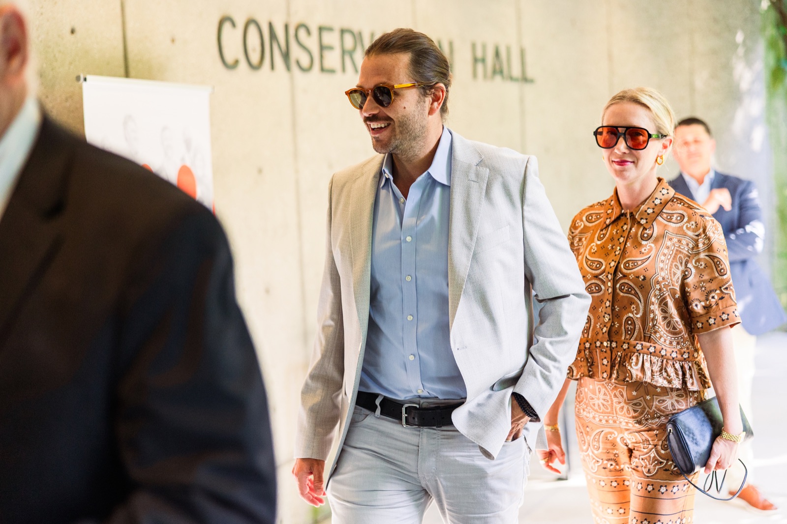 A couple in sunglasses walking into Conservation Hall, smiling