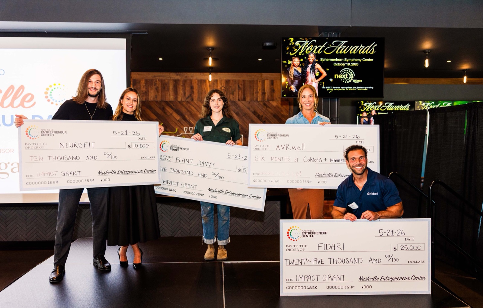Spring 2026 Impact Grant winners on stage holding oversized checks
