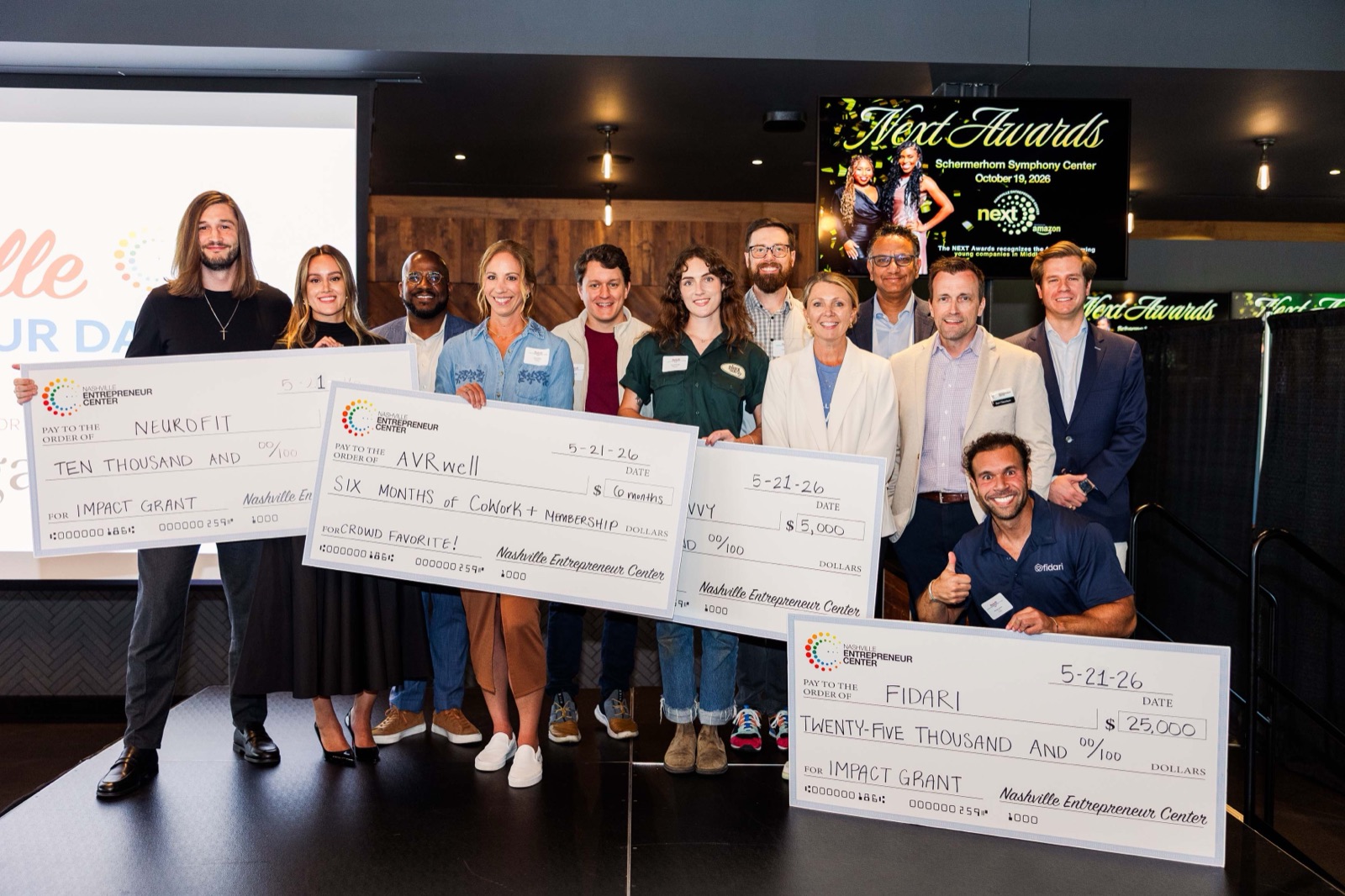 Spring 2026 Impact Grant winners on stage holding oversized checks