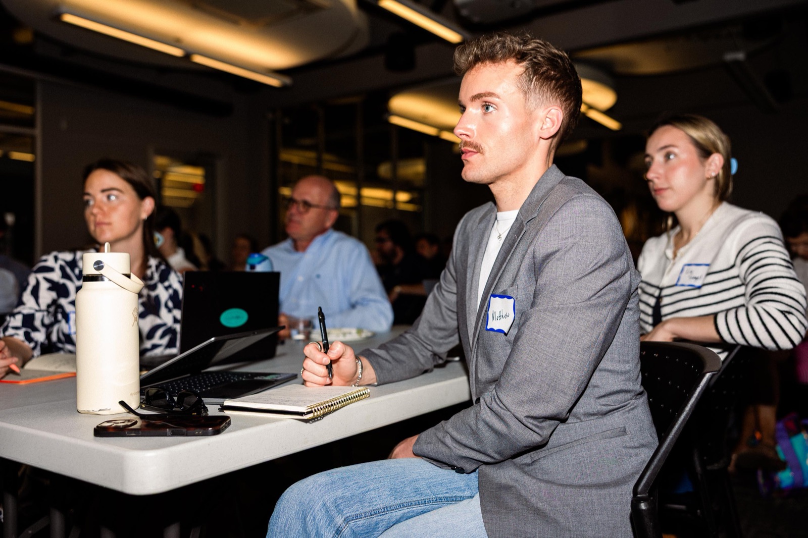 A TakeOff founder taking notes at a laptop during a cohort session at the EC, with the rest of the cohort seated behind