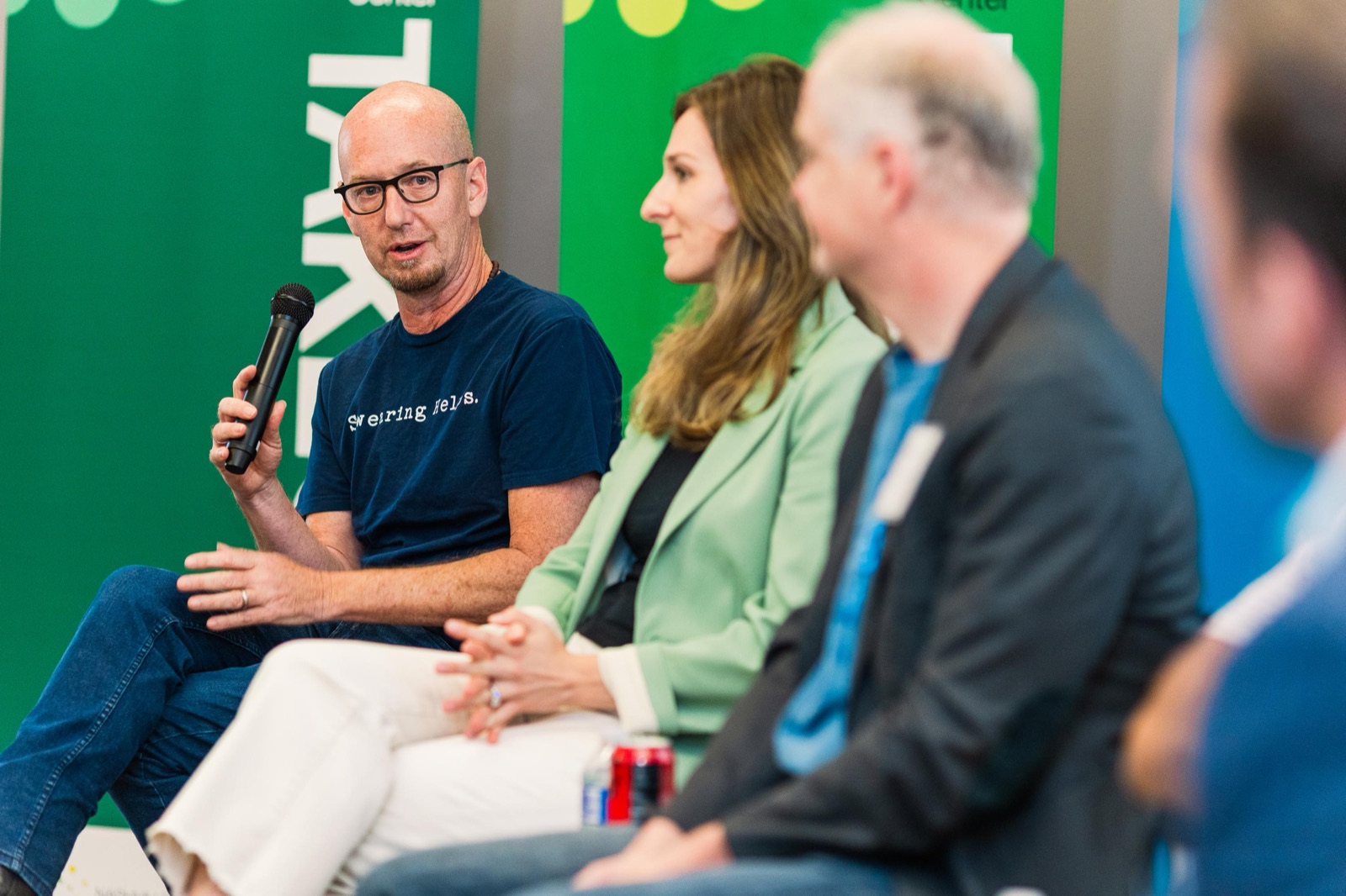 Speakers with a microphone in front of a TakeOff banner during a cohort session