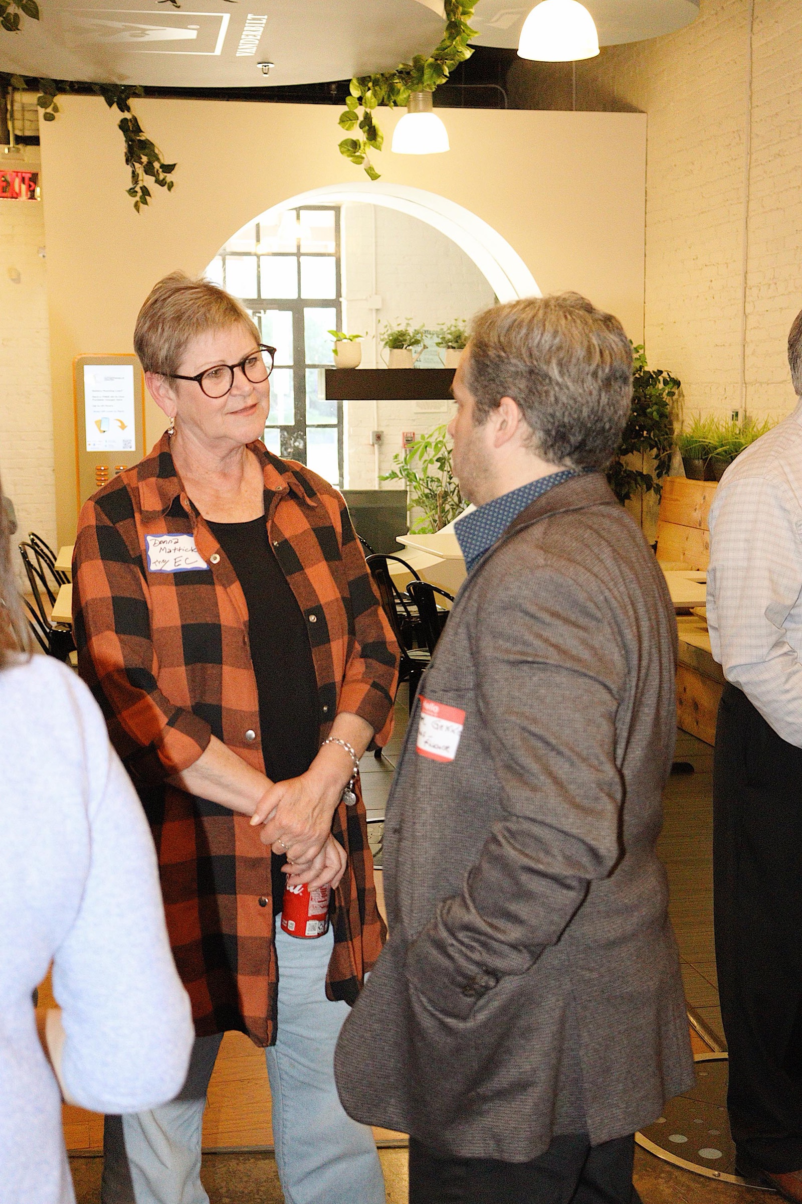 Donna Mattick in a plaid shirt and name tag talking with a guest in the EC lobby